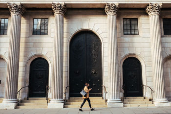 person walking past the exterior of a classical building