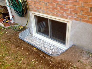 basement window with a metal egress window well filled with gravel