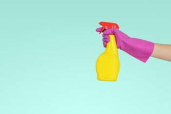 A hand wearing a pink rubber glove holding a bright yellow spray bottle